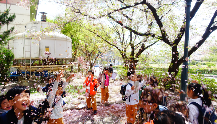 바람에 흩날리는 벚꽃나무 아래에서 어린이들이 즐거워 하고 있다