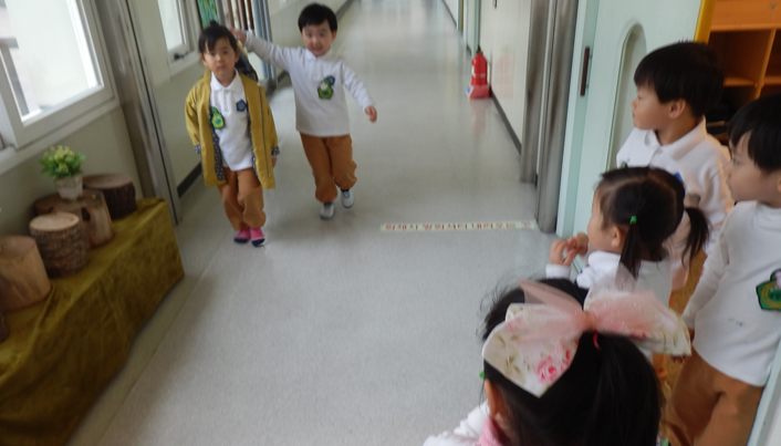 복도를 걸어오는 두 명의 아이들과 교실에서 나와 그 둘을 보고 있는 아이들의 모습이다
