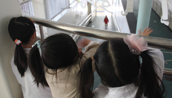 윗층에 서 있는 세 명의 여자아이들이 1층의 복도에 서있는 친구를 향해 손을 흔들고 있는 모습이다