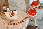 산타모자와 망토 마스크를 하고있는 기린 인형 옆에 테이블 위에 크리스마스 장식물이 장식되어있다.