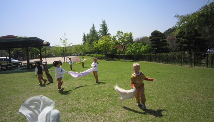 아이들이 한 손에는 천을 들고 잔디밭을 달리고 있는 모습이다