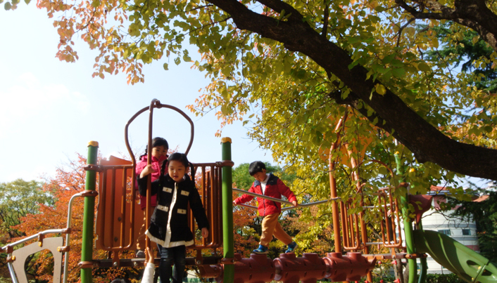 단풍나무 아래에서 놀이터의 놀이기구를 즐기고 있는 아이들의 모습이다