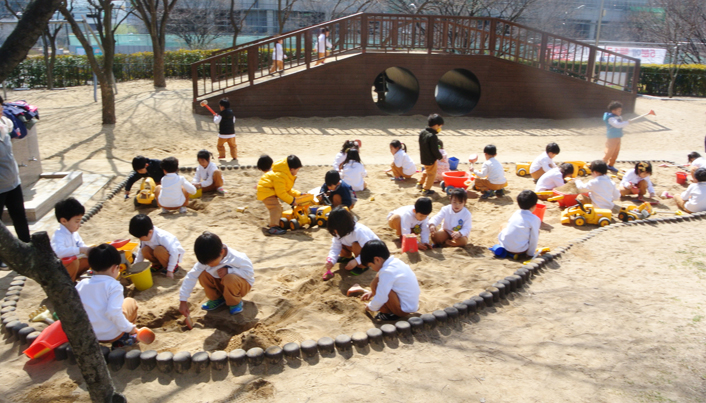 많은 아이들이 모래위에 쭈그리고 앉아 삽을 이용해 모래놀이를 하고 있는 모습이다