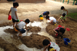 물이 흐르고 있는 모래사장 위에서 아이들이 삽과 통을 들고 모래놀이를 하고 있는 모습이다