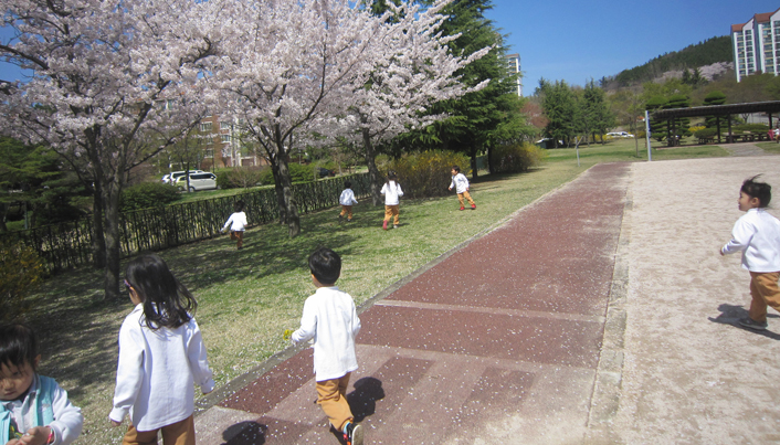운동장에 피어있는 벚꽃나무 아래로 아이들이 달려가는 모습이다