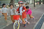헬멧을 쓴 남자어린이가 자전거를 타고 여자아이들이 뒤에서 밀고 있다