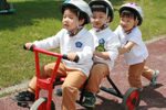 남자아이 둘이 빨간 자전거에 앞뒤로 함께 타고 있고, 뒤에서 다른 남자아이가 자전거를 밀고 있는 사진이다