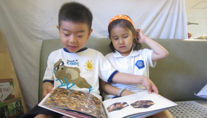 소파에 앉아 책 한 권을 같이 보고 있는 남자아이와 여자아이의 모습이다