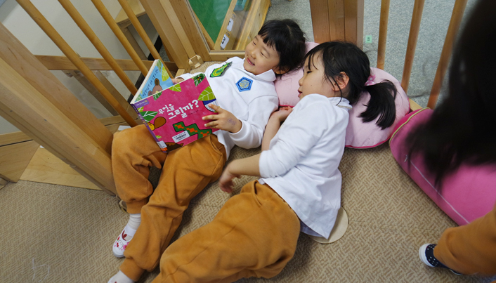 카펫위에 두 여자 어린이가 누워 함께 책을 보고 있다