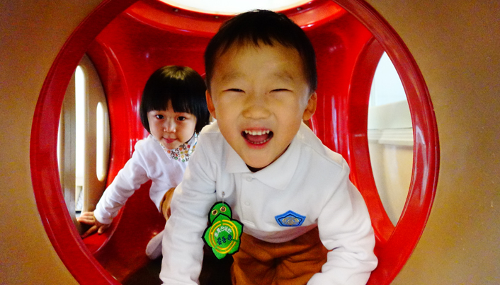 놀이시설 안에서 카메라를 보고 환하게 웃고 있는 남자아이와 여자아이의 모습이다