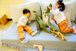 소파에 앉아 공룡인형을 갖고 놀고 있는 남자아이와 여자아이의 모습이다