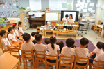 아이들이 의자에 앉아 교실 앞에서 선생님과 한 친구가 실험을 하는 모습을 지켜보고 있다